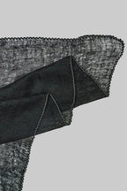 A close-up of a black sheer cashmere scarf with a white stitch edge, on a light gray background.