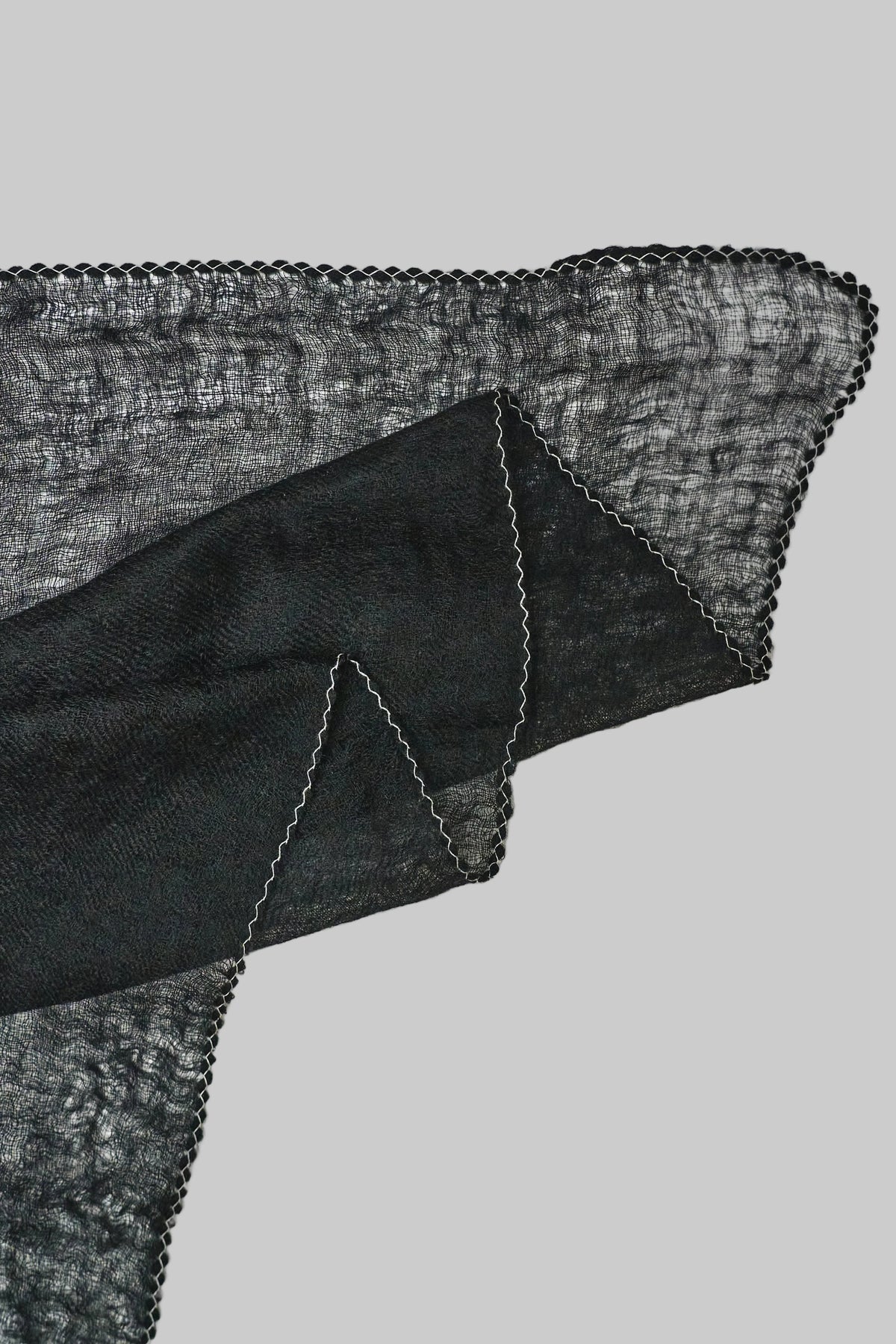 A close-up of a black sheer cashmere scarf with a white stitch edge, on a light gray background.