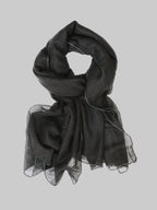 A lightweight black cashmere scarf with delicate white stitch edges, draped in a looped style against a light gray background.