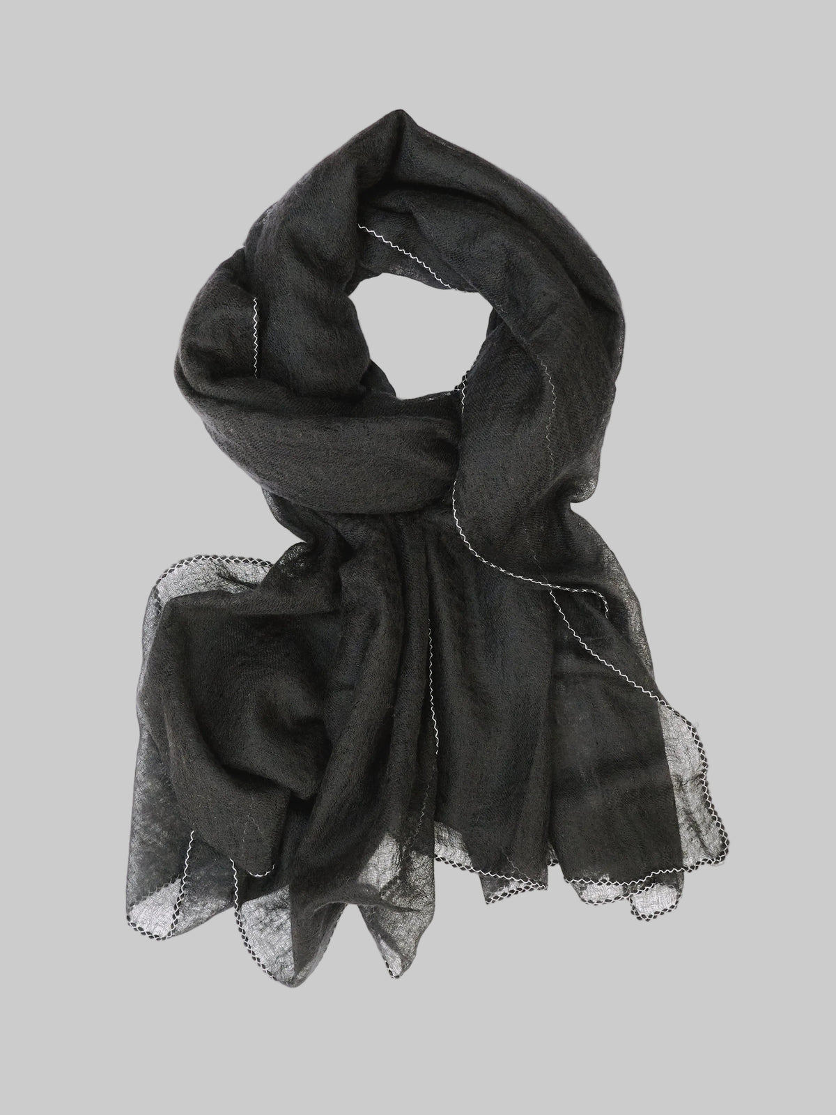 A lightweight black cashmere scarf with delicate white stitch edges, draped in a looped style against a light gray background.